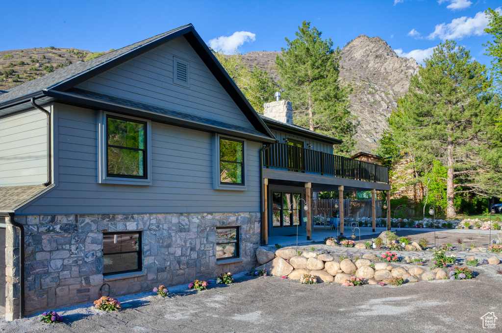 Back of house with a patio area, a chimney, stone siding, roof with shingles, and a deck with mountain view