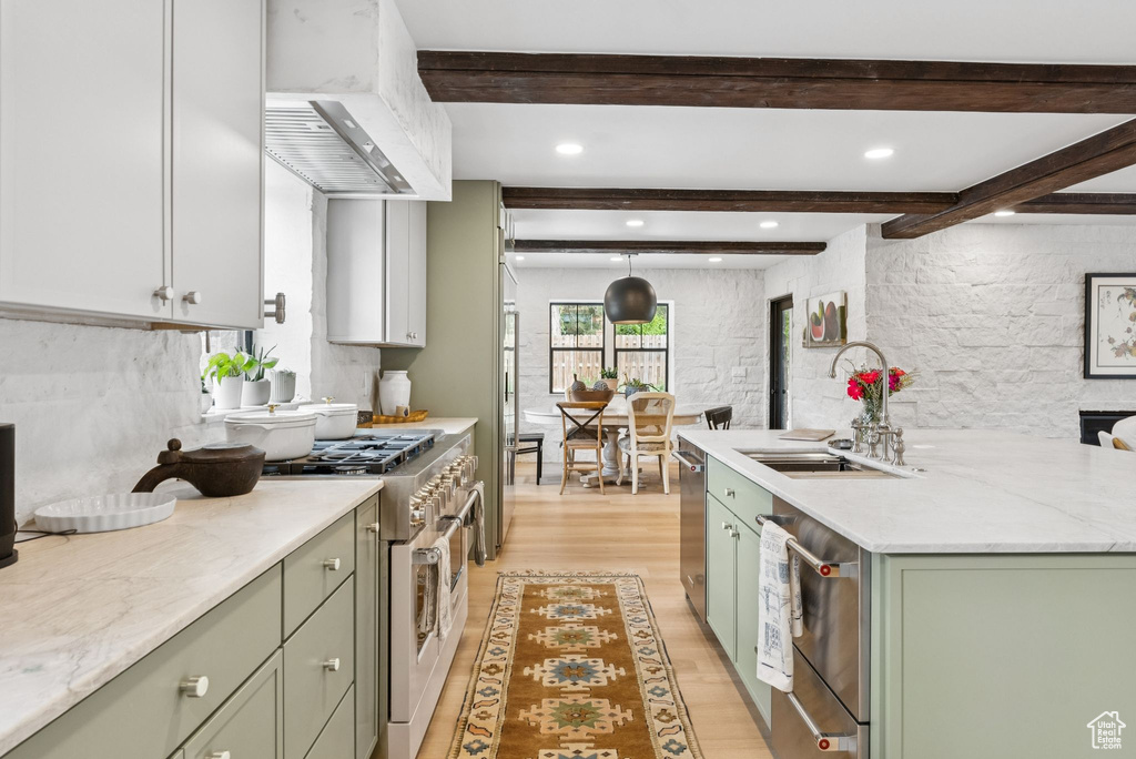 Kitchen featuring green cabinetry, appliances with stainless steel finishes, light wood-style floors, custom range hood, and beam ceiling
