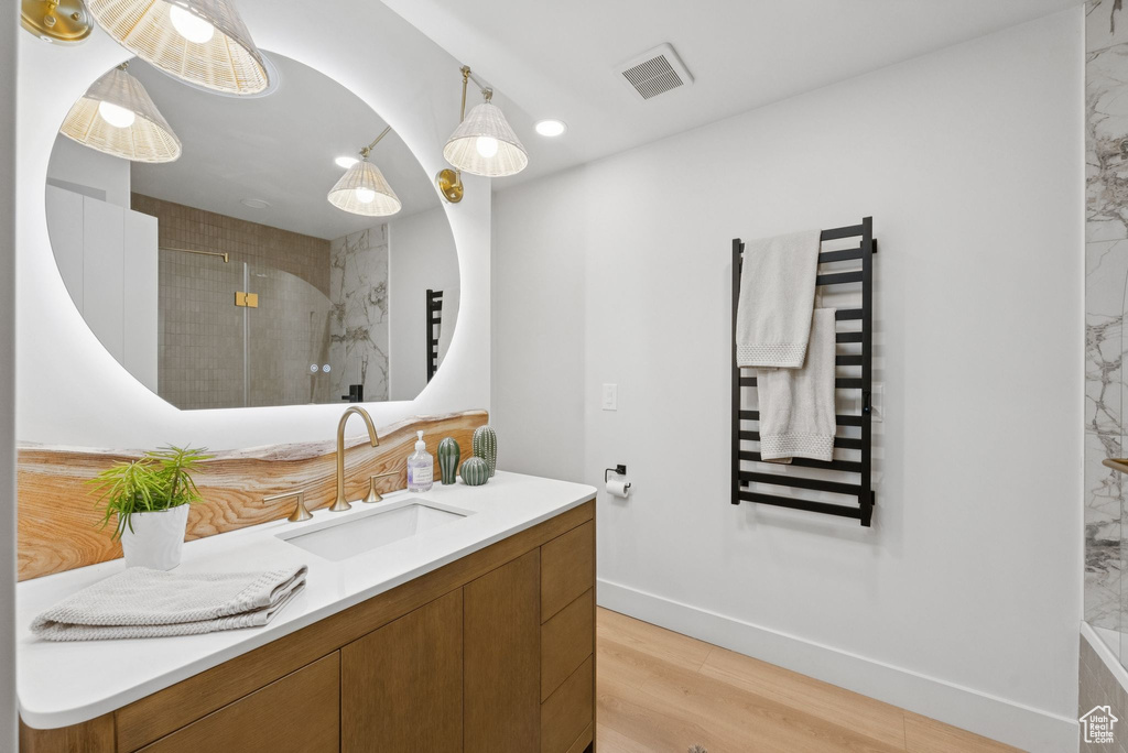 Bathroom with a towel warmer, vanity, wood finished floors, and a shower