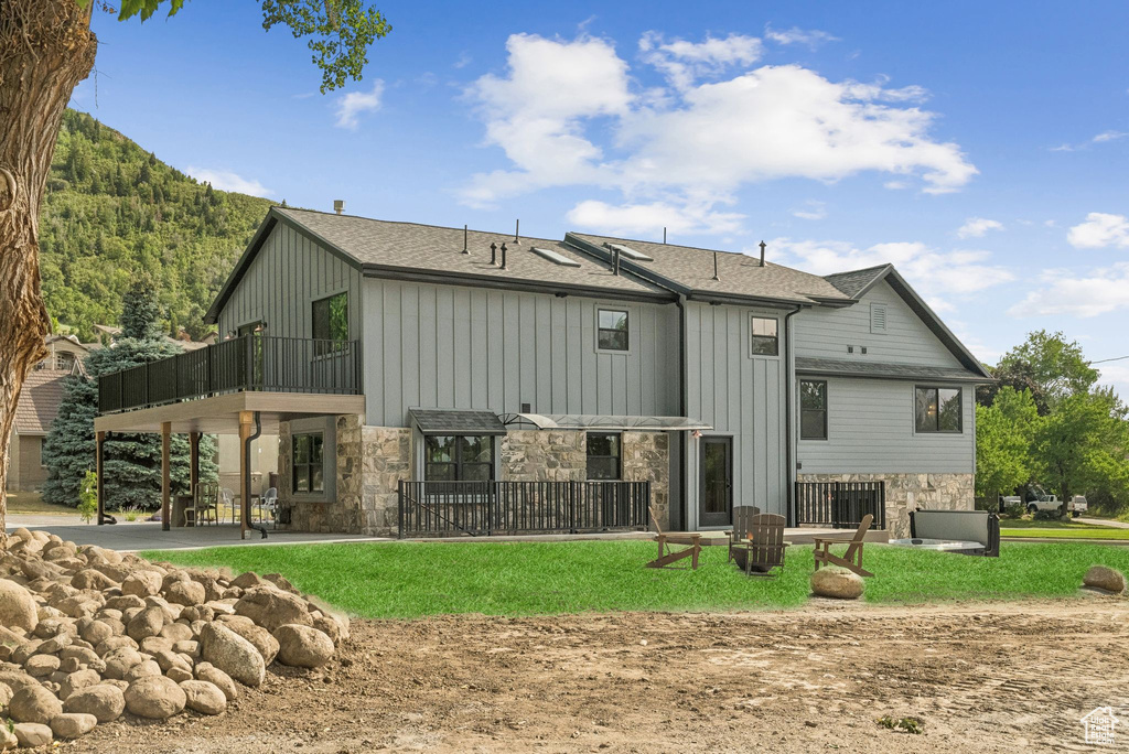 Rear view of house with stone siding, board and batten siding, a balcony, a patio, and a lawn