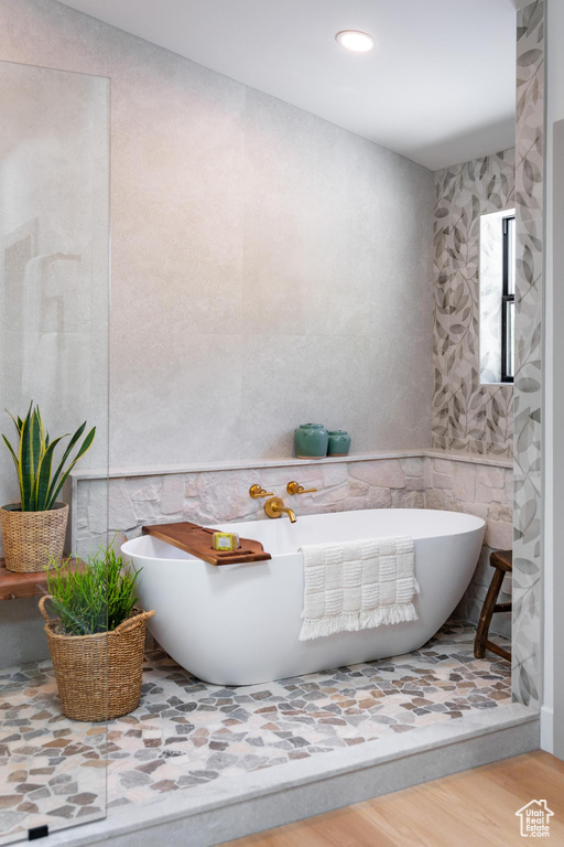 Full bathroom featuring a freestanding bath, wood finished floors, tile walls, and recessed lighting