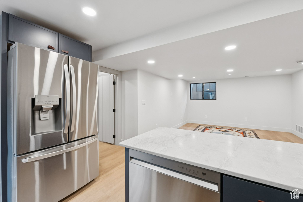 Kitchen with appliances with stainless steel finishes, light stone counters, light wood-type flooring, and recessed lighting