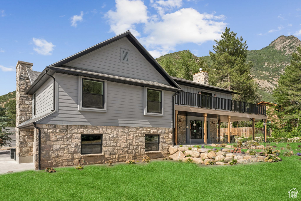 Rear view of house featuring a chimney, stone siding, a yard, and a deck with mountain view
