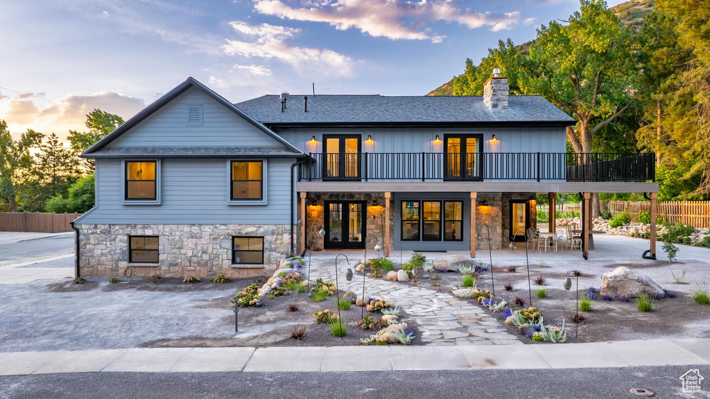 View of front of house with french doors, stone siding, a chimney, a patio area, and a balcony
