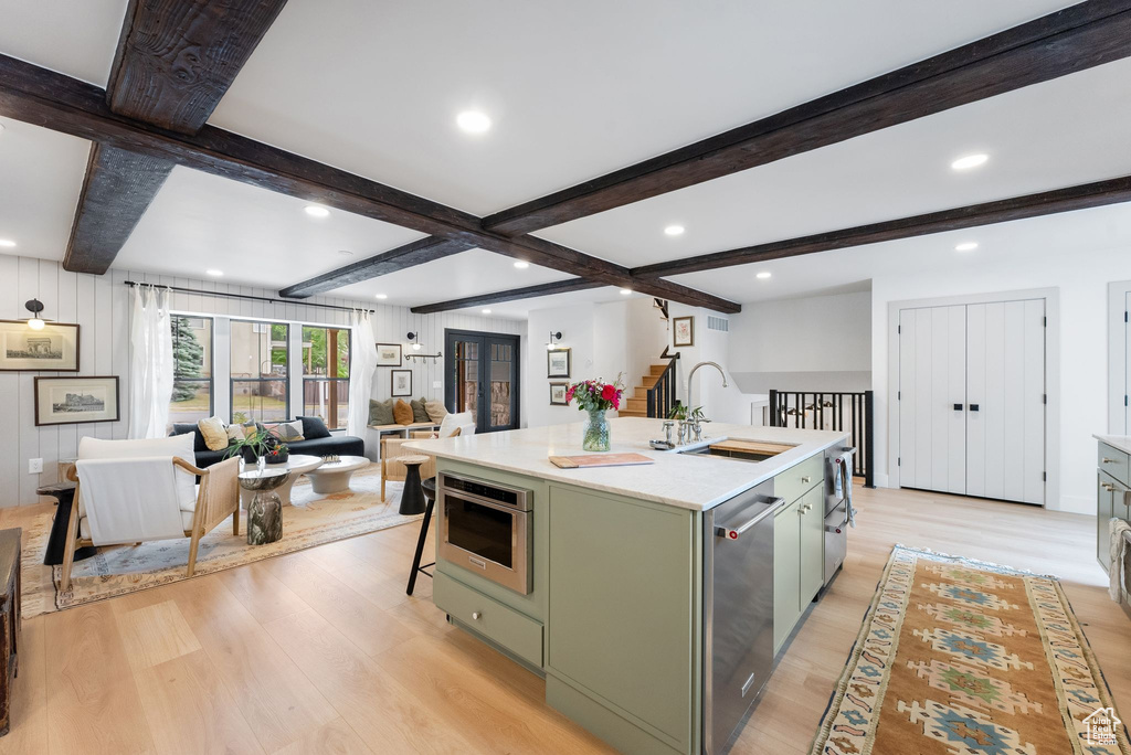 Kitchen with green cabinetry, light wood finished floors, dishwasher, light countertops, and open floor plan