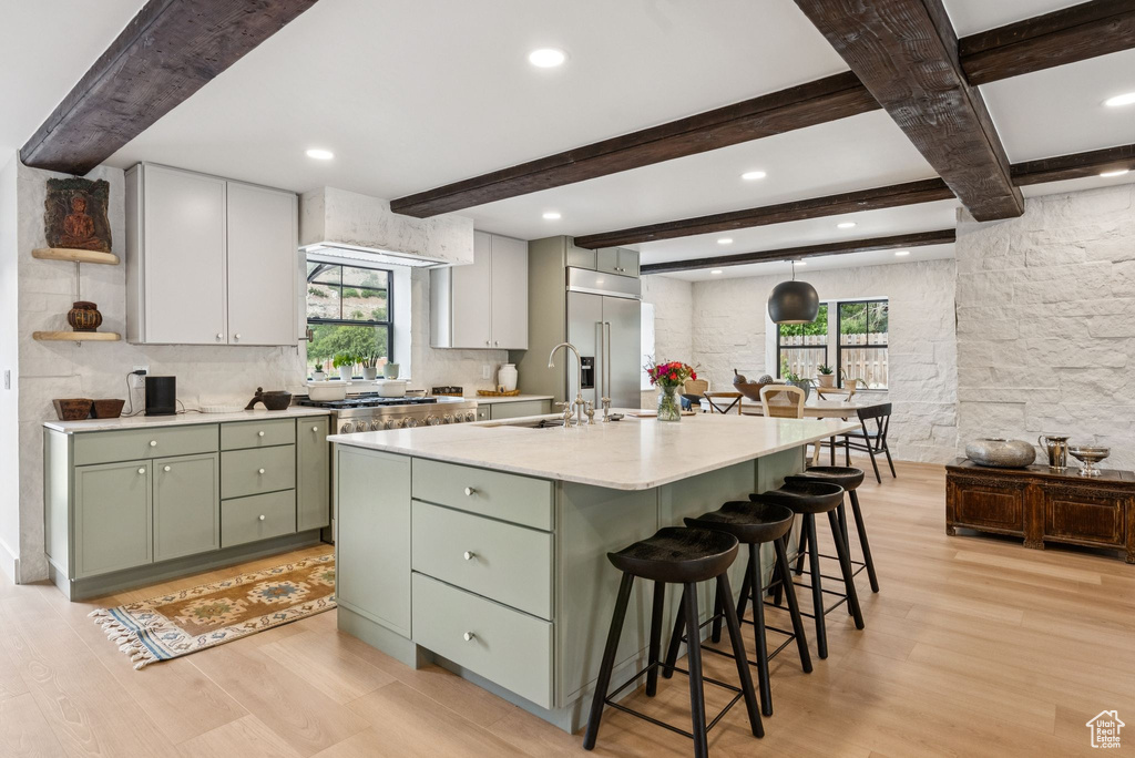 Kitchen with green cabinets, stainless steel appliances, light wood-style floors, backsplash, and beamed ceiling