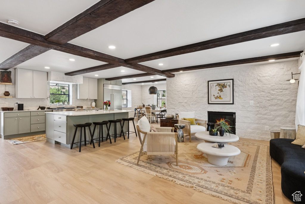 Living room featuring beamed ceiling, light wood-type flooring, a fireplace, and recessed lighting