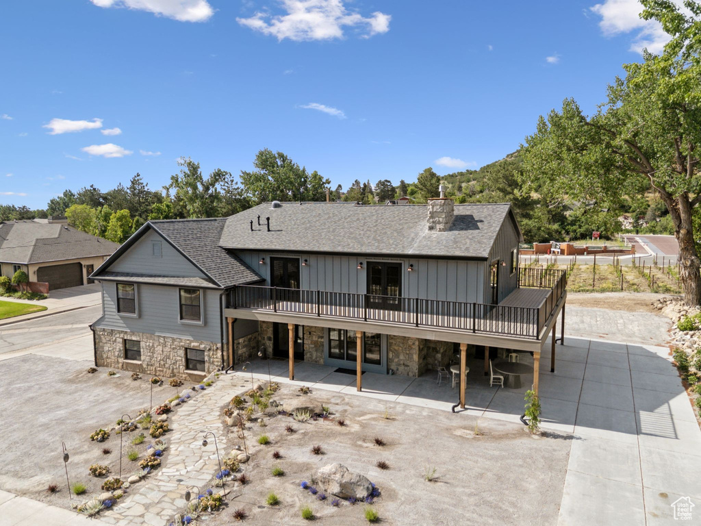 Back of house with stone siding, roof with shingles, a wooden deck, and board and batten siding