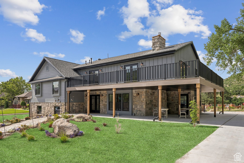 Back of house with a lawn, stone siding, board and batten siding, a chimney, and a patio