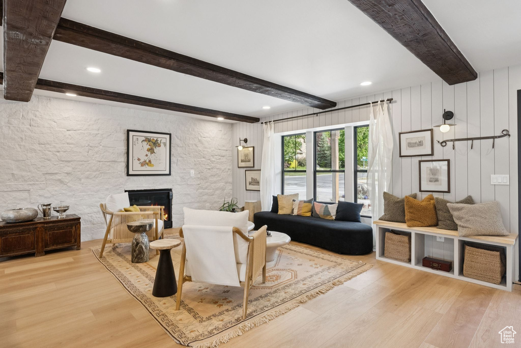 Living room featuring wood finished floors, beam ceiling, a stone fireplace, and recessed lighting