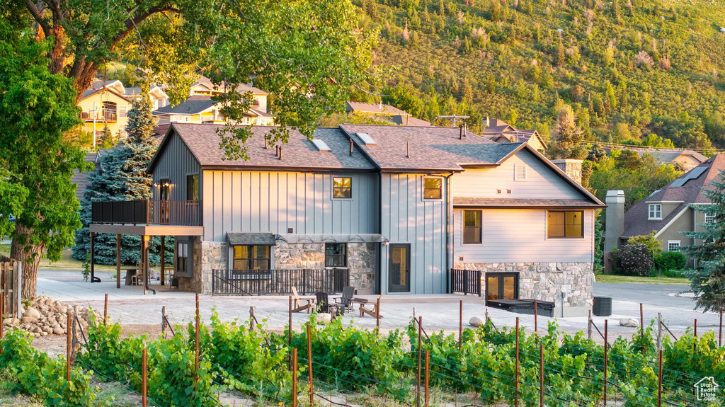 Back of house with stone siding, board and batten siding, a patio area, a shingled roof, and a balcony