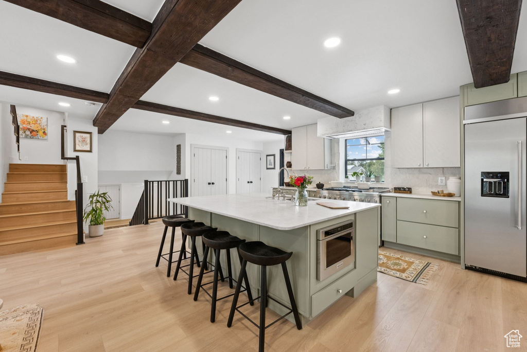 Kitchen with stainless steel built in fridge, light wood-type flooring, beamed ceiling, a kitchen bar, and light countertops
