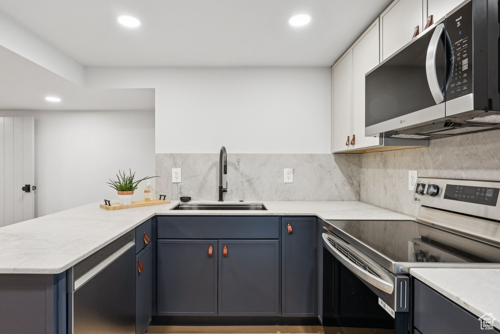 Kitchen with stainless steel appliances, a peninsula, recessed lighting, decorative backsplash, and white cabinetry
