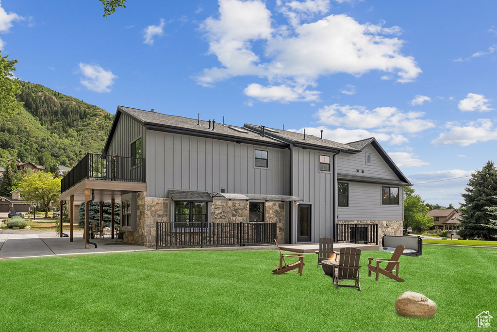 Rear view of property featuring stone siding, a yard, board and batten siding, and a balcony