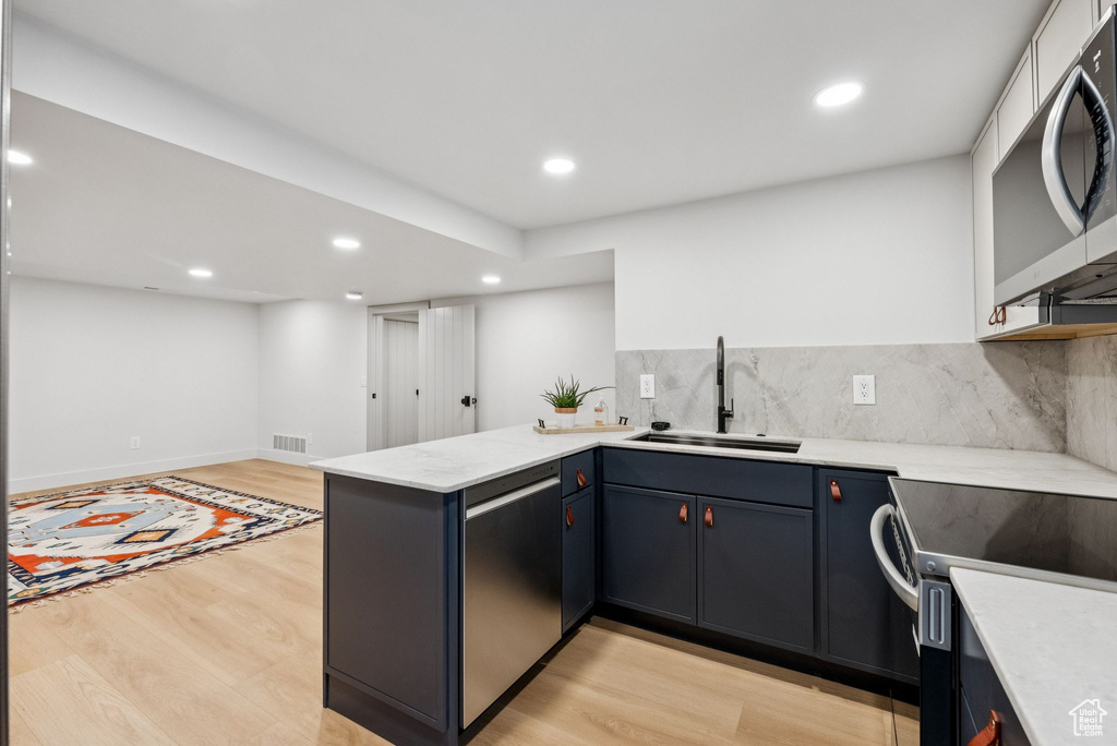 Kitchen featuring a peninsula, stainless steel appliances, light wood finished floors, recessed lighting, and backsplash
