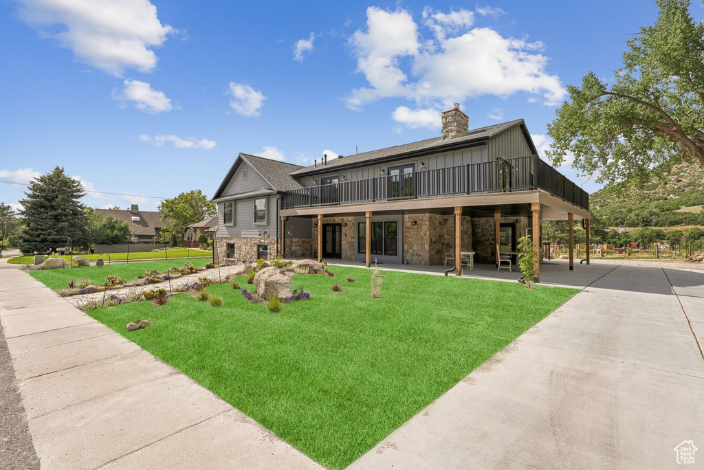 Rear view of property featuring a wooden deck, a chimney, stone siding, and a patio area