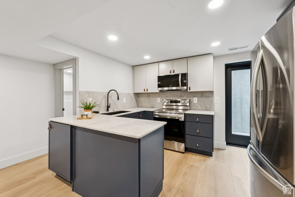 Kitchen with appliances with stainless steel finishes, white cabinetry, a peninsula, tasteful backsplash, and light wood-style floors