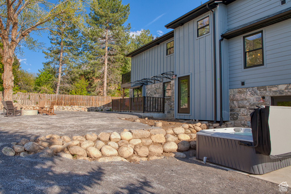 View of side of home with board and batten siding, a hot tub, a patio area, and stone siding