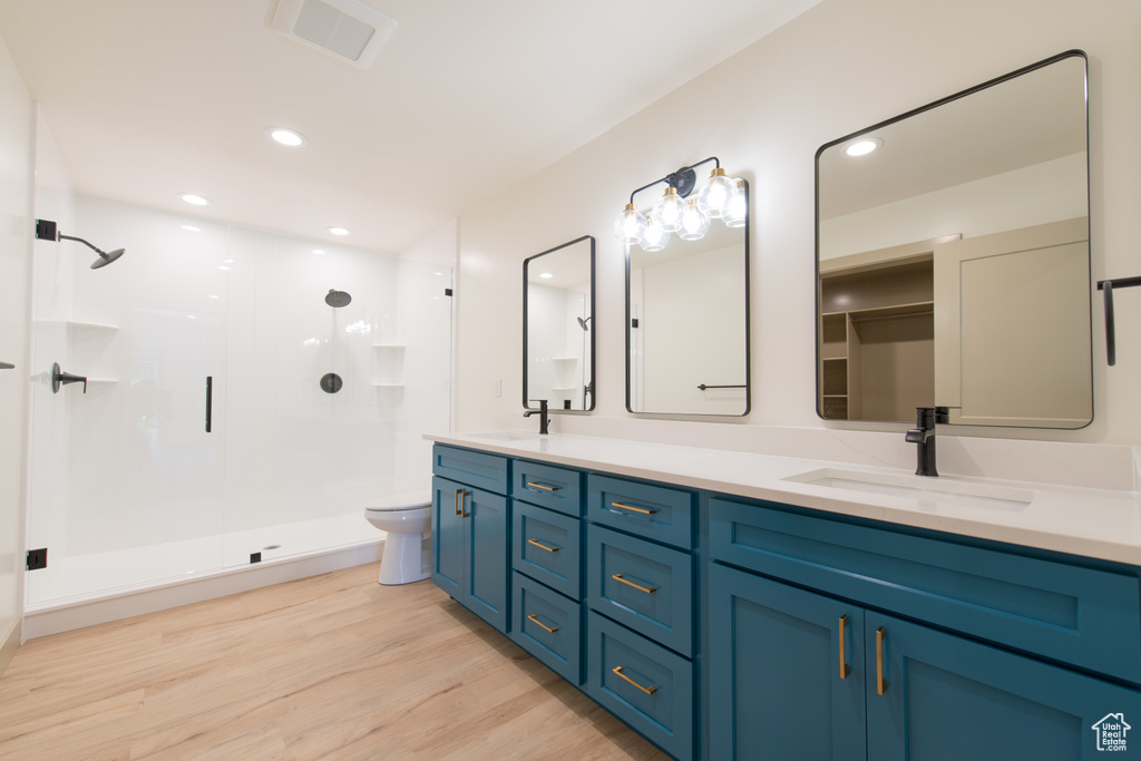 Bathroom featuring a stall shower, wood finished floors, double vanity, toilet, and recessed lighting