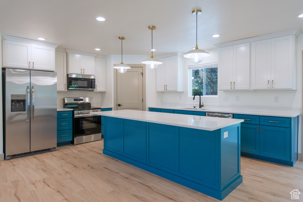 Kitchen featuring stainless steel appliances, blue cabinetry, a sink, a kitchen island, and light countertops