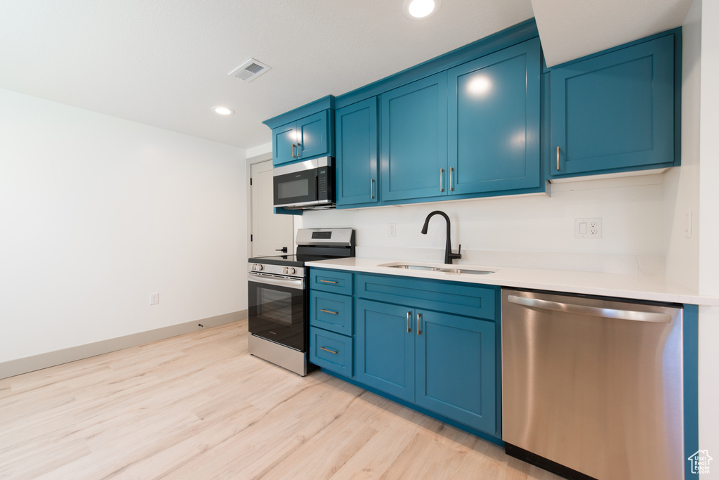 Kitchen with appliances with stainless steel finishes, a sink, blue cabinets, light wood finished floors, and light countertops