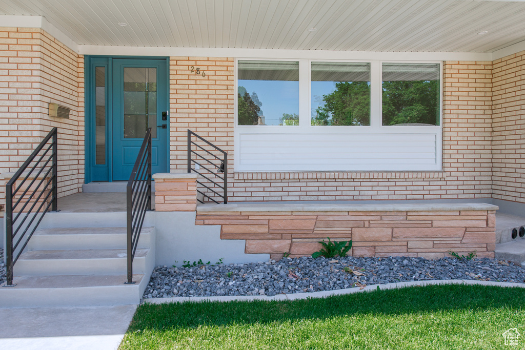 View of exterior entry featuring brick siding and a porch