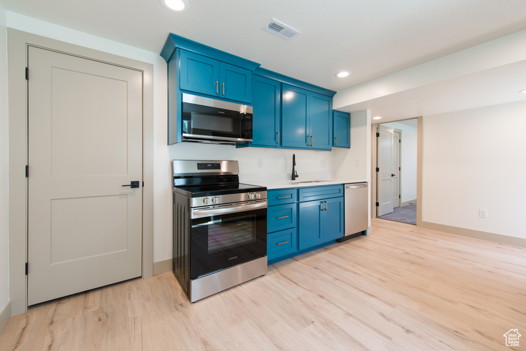 Kitchen featuring appliances with stainless steel finishes, blue cabinets, light wood-type flooring, a sink, and recessed lighting