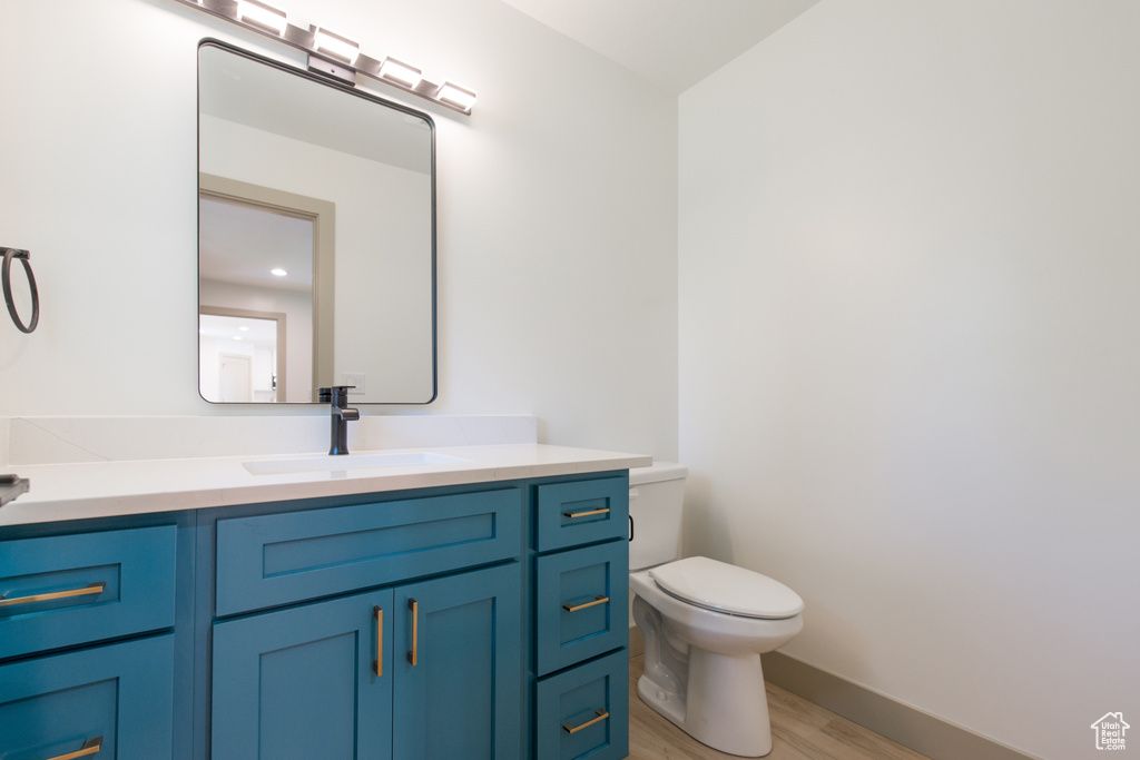 Half bath with wood finished floors, toilet, vanity, and baseboards