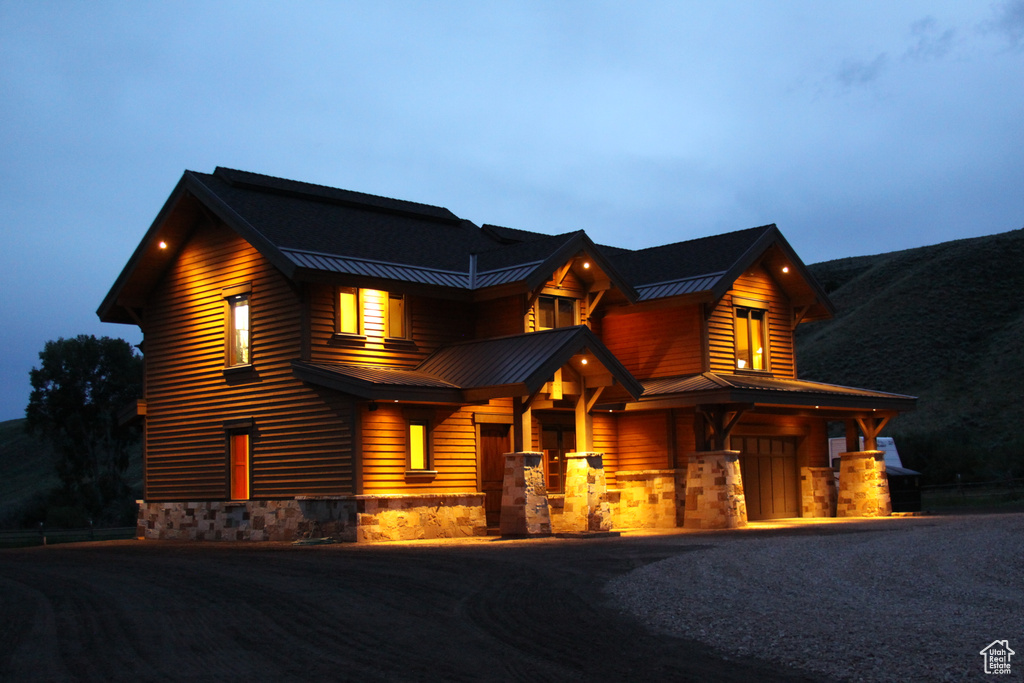 View of front of house featuring a standing seam roof, a garage, stone siding, metal roof, and driveway