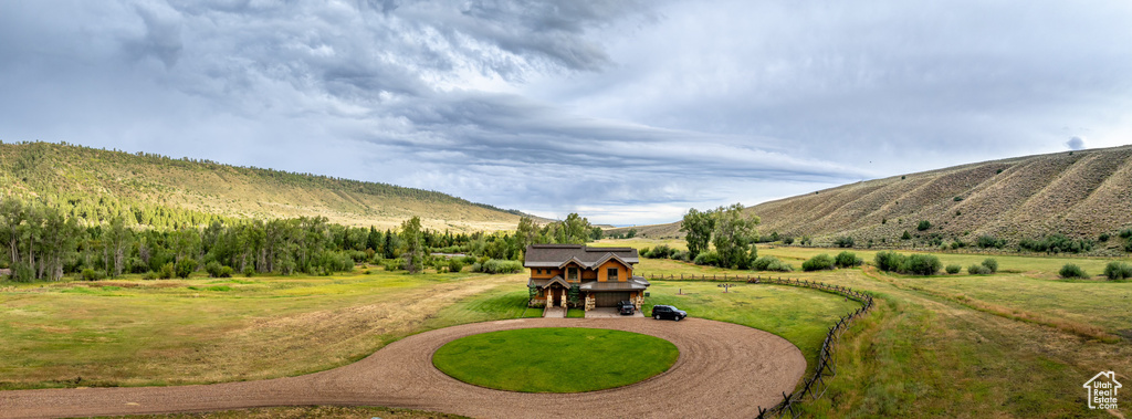 View of grassy yard featuring curved driveway, a rural view, and a mountain view