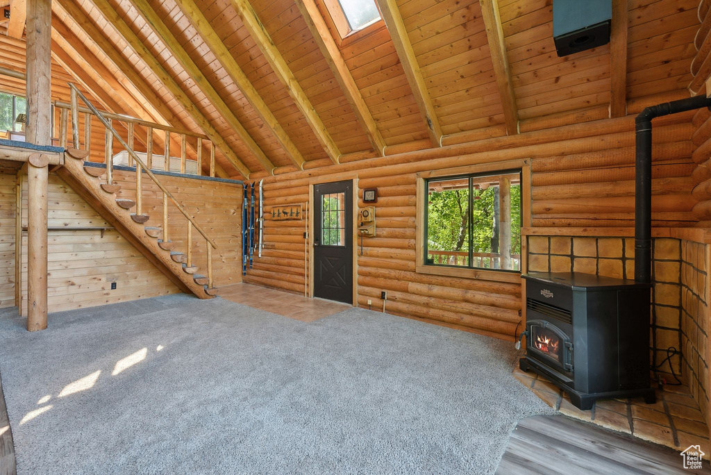 Unfurnished living room featuring a wood stove, healthy amount of natural light, wooden ceiling with exposed beams, high vaulted ceiling, and stairway