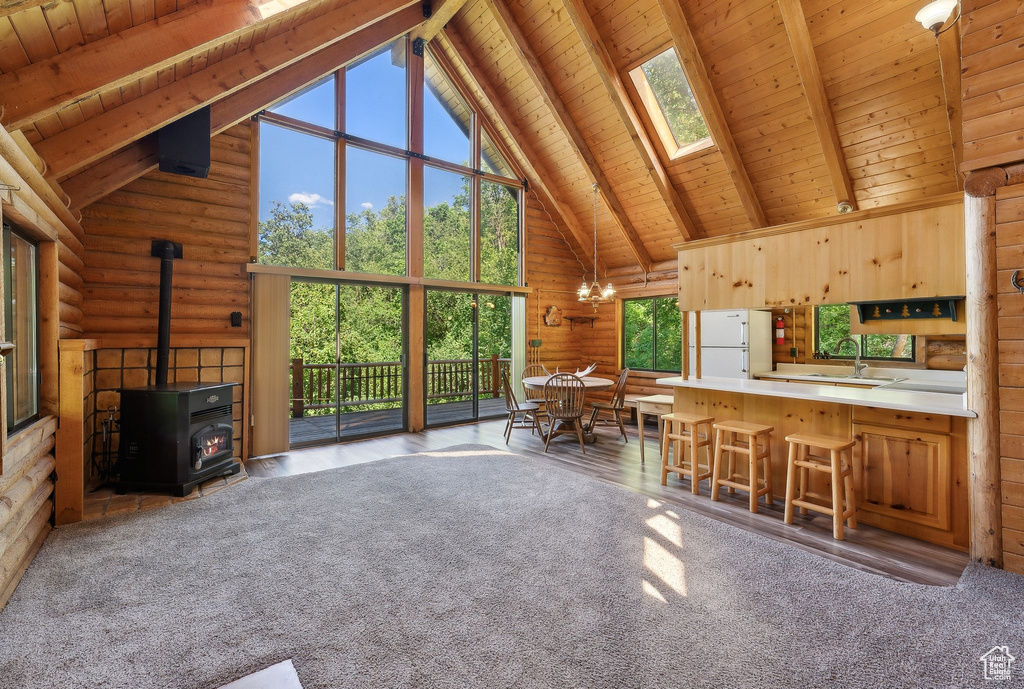 Unfurnished living room featuring wooden ceiling with exposed beams, a sink, high vaulted ceiling, a wood stove, and a skylight