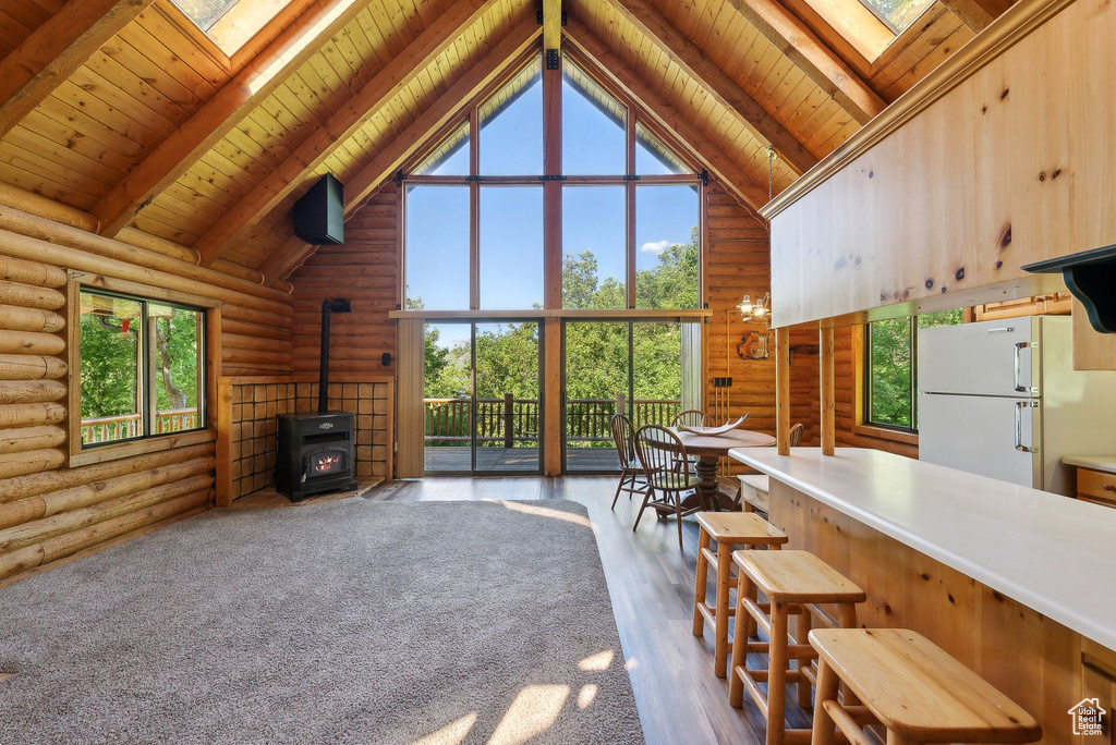 Living area featuring rustic walls, a wood stove, a skylight, high vaulted ceiling, and wooden ceiling with exposed beams