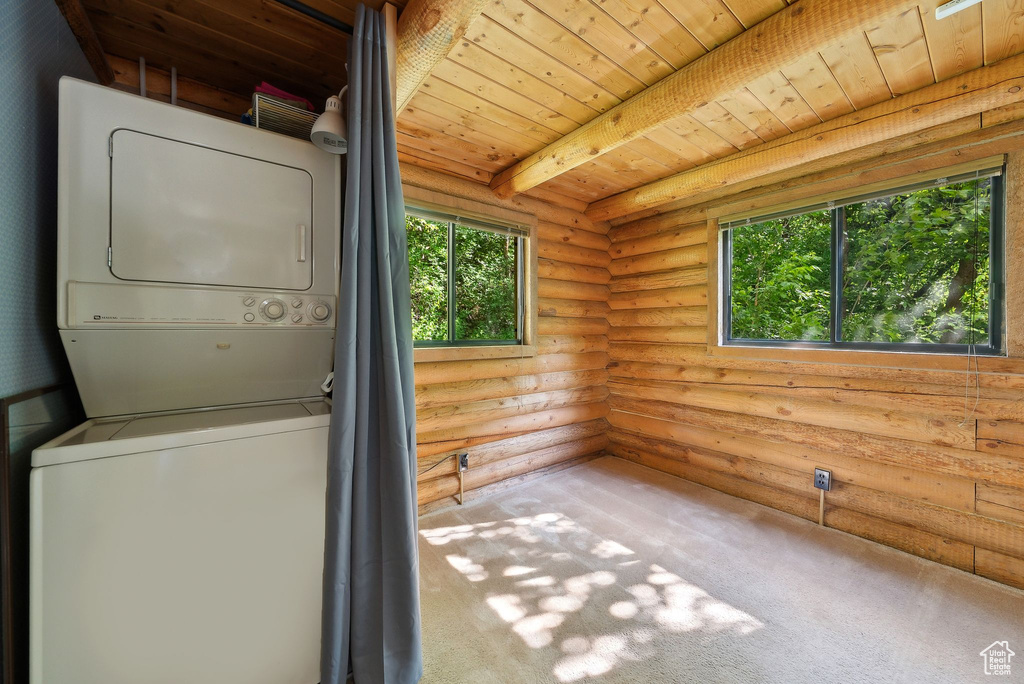 Washroom with stacked washer and clothes dryer, rustic walls, wooden ceiling, and carpet flooring