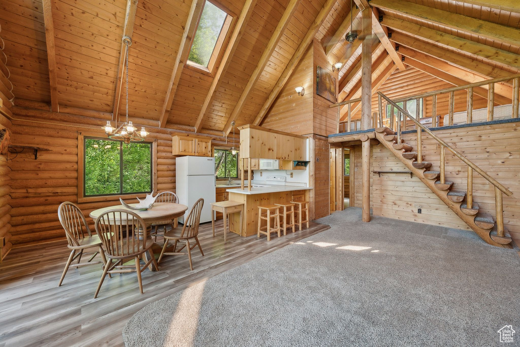 Dining space with high vaulted ceiling, a skylight, a chandelier, wooden ceiling with exposed beams, and light wood-style flooring