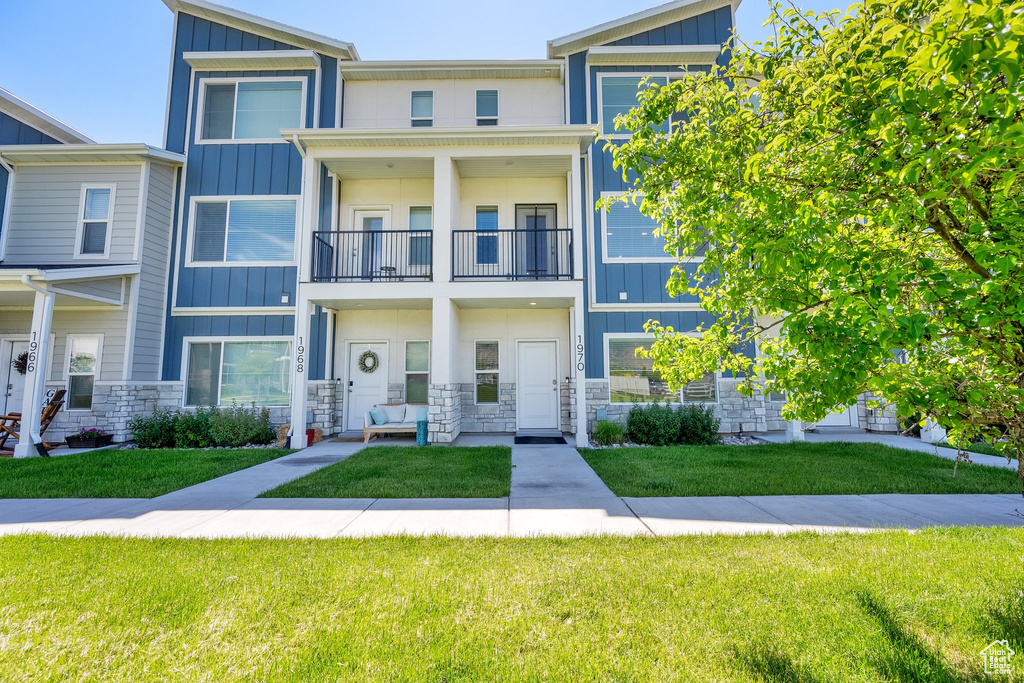 Townhome / multi-family property with board and batten siding, a balcony, stone siding, and a front lawn
