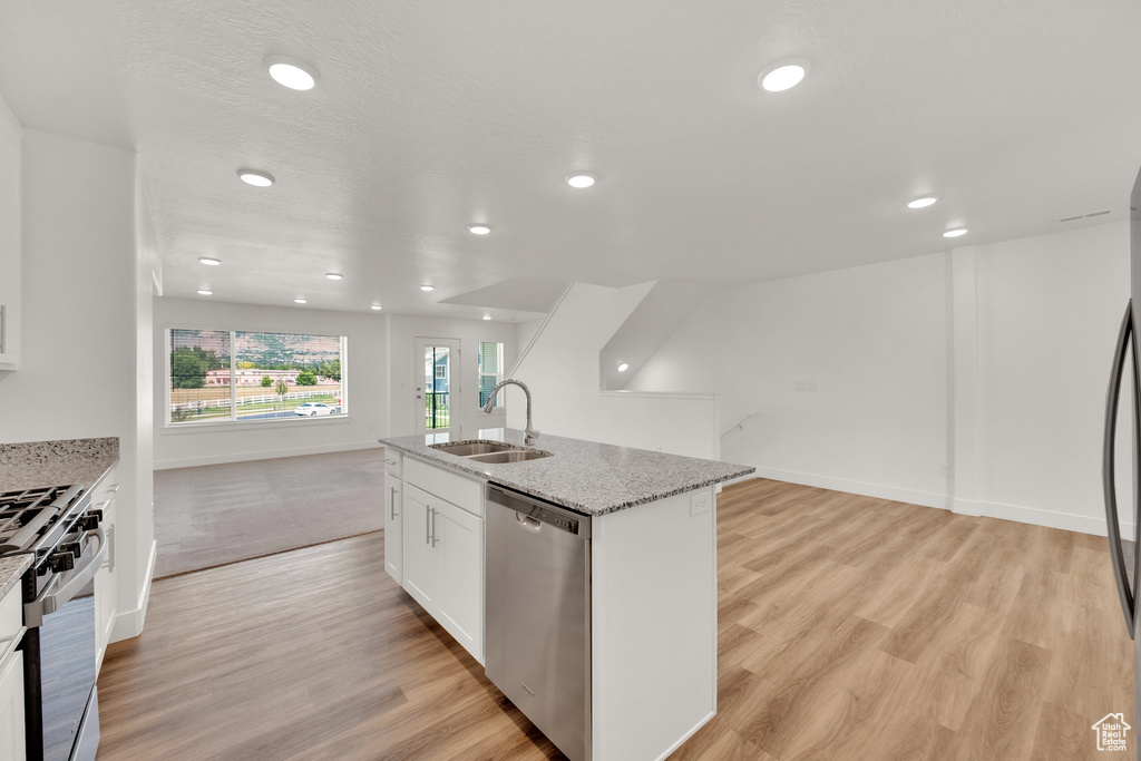 Kitchen featuring stainless steel appliances, a sink, open floor plan, an island with sink, and light wood-style floors