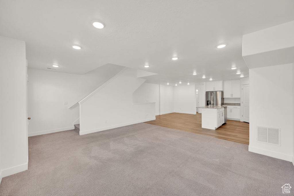 Unfurnished living room featuring light carpet, recessed lighting, baseboards, and stairs
