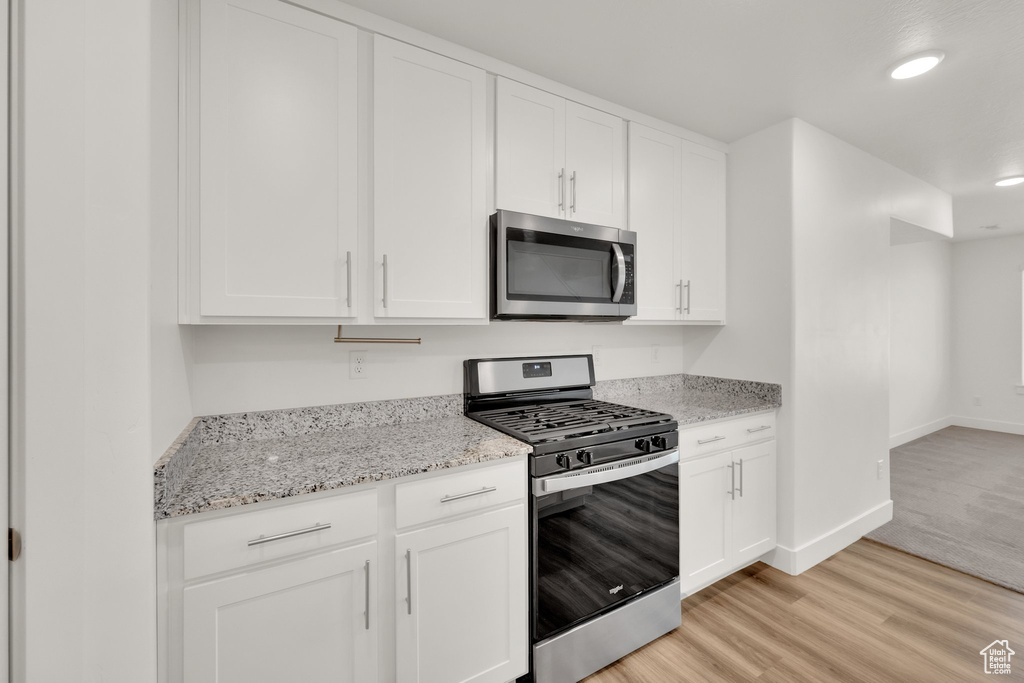 Kitchen with appliances with stainless steel finishes, light wood finished floors, white cabinetry, and recessed lighting