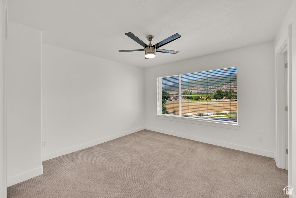 Spare room with a ceiling fan, light carpet, and baseboards