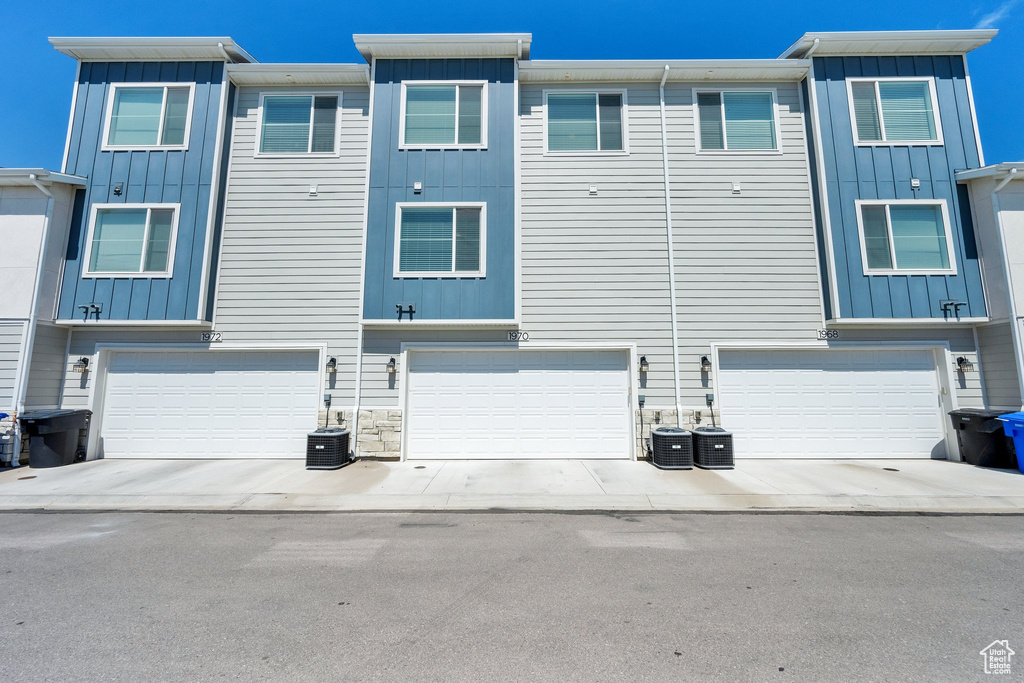 Rear view of house with board and batten siding, an attached garage, and central AC unit