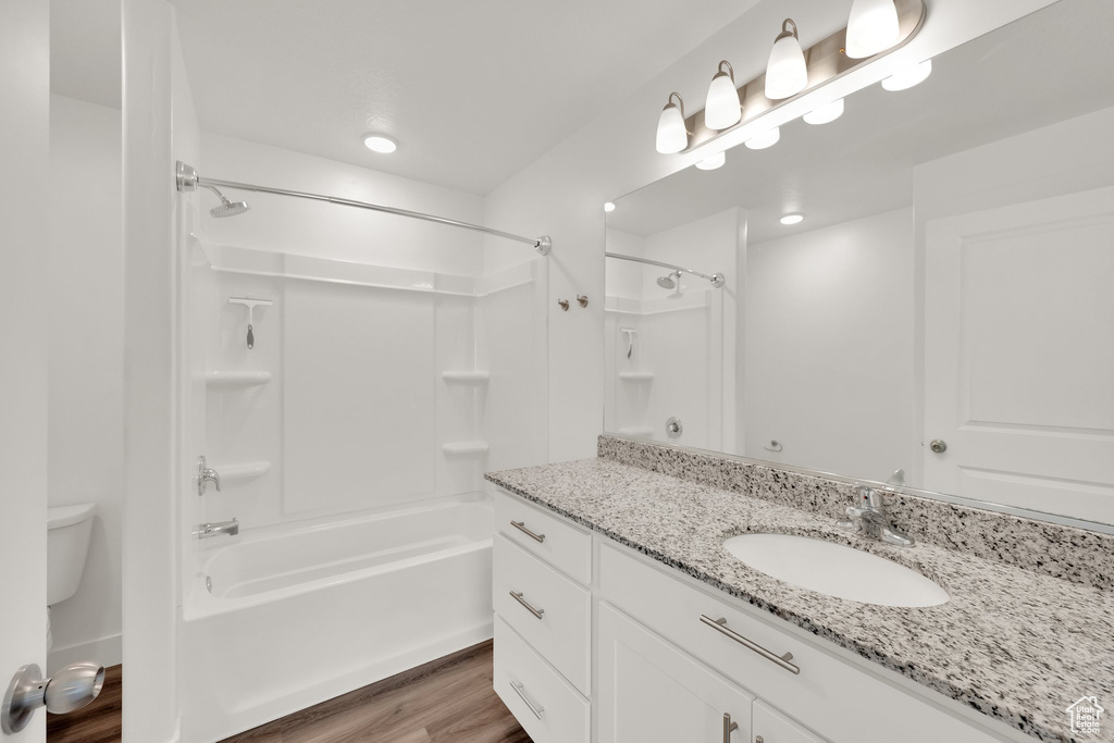 Bathroom featuring wood finished floors, shower / bath combination, vanity, and toilet