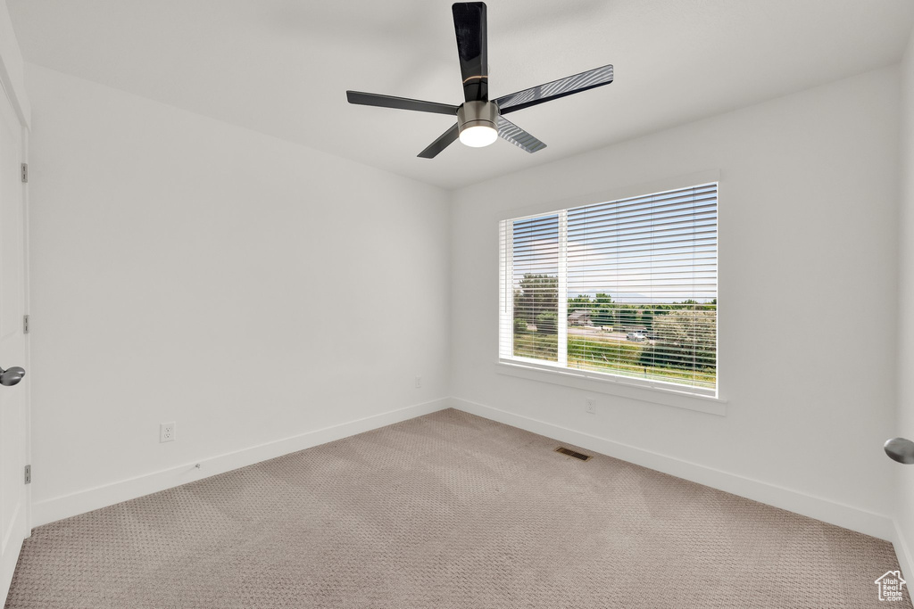 Empty room featuring light colored carpet, baseboards, and a ceiling fan