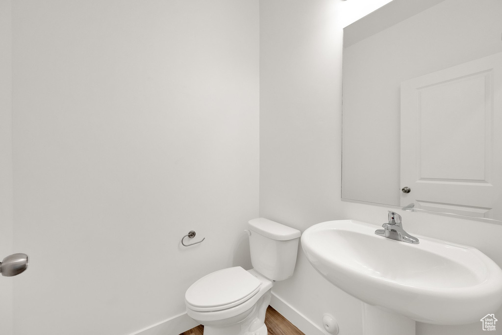 Half bathroom with wood finished floors, baseboards, toilet, and a sink