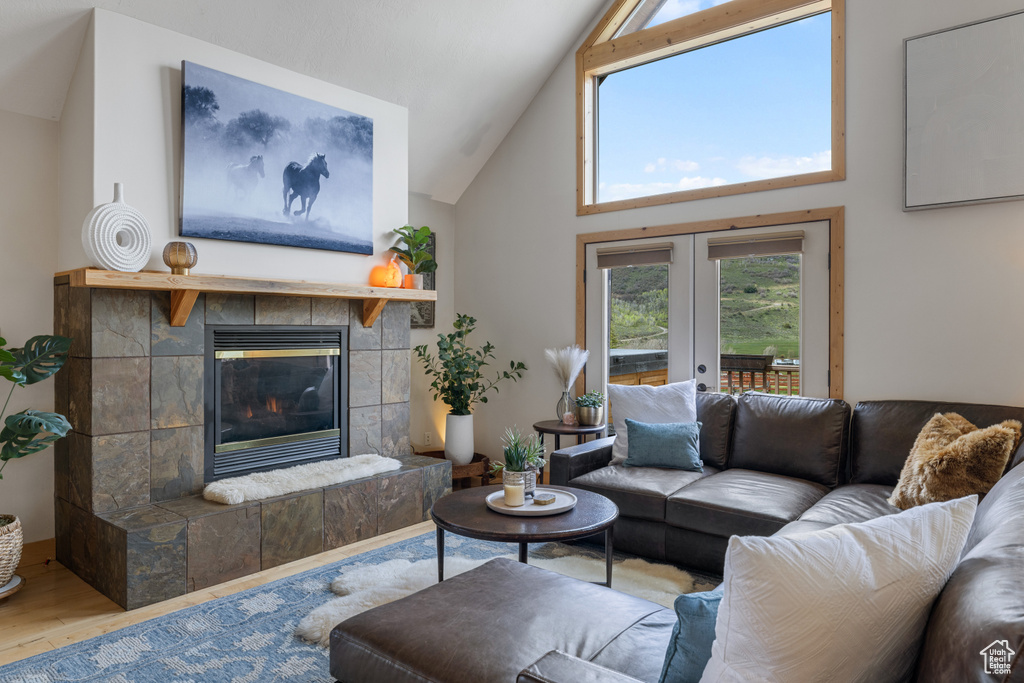 Living room featuring wood finished floors, a tile fireplace, high vaulted ceiling, and french doors