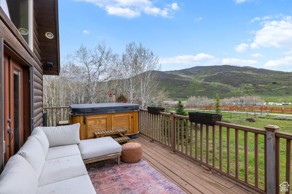 Wooden terrace featuring a hot tub, a mountain view, and a lawn