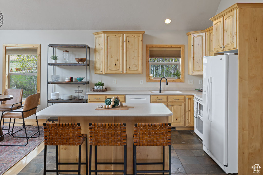 Kitchen featuring light brown cabinetry, white appliances, a sink, and recessed lighting
