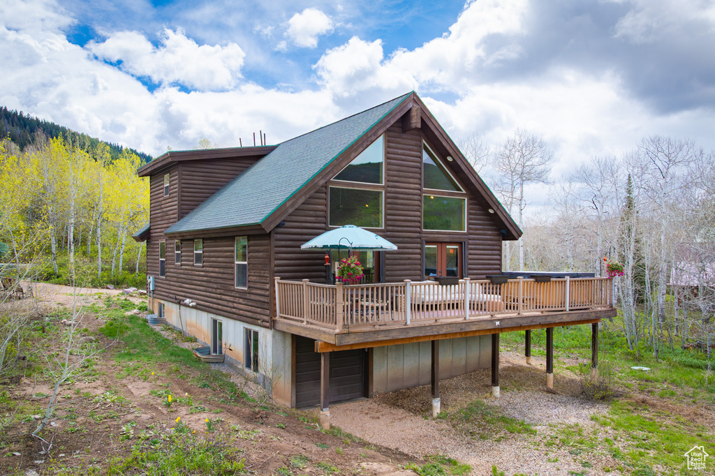Back of house with a deck, dirt driveway, and a view of trees