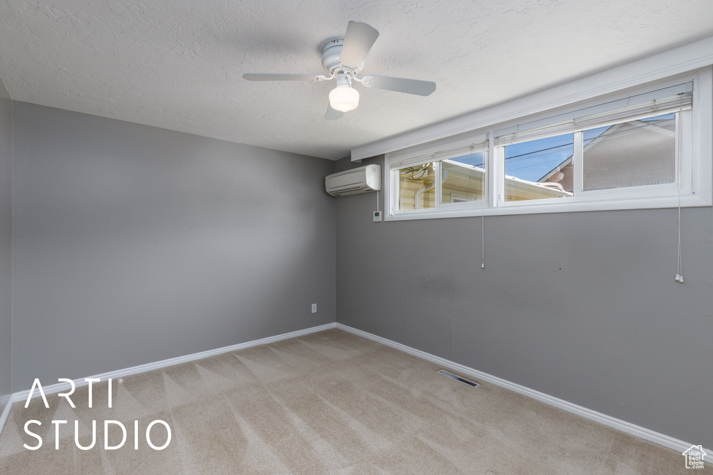 Empty room featuring a wall unit AC, light colored carpet, a ceiling fan, baseboards, and a textured ceiling