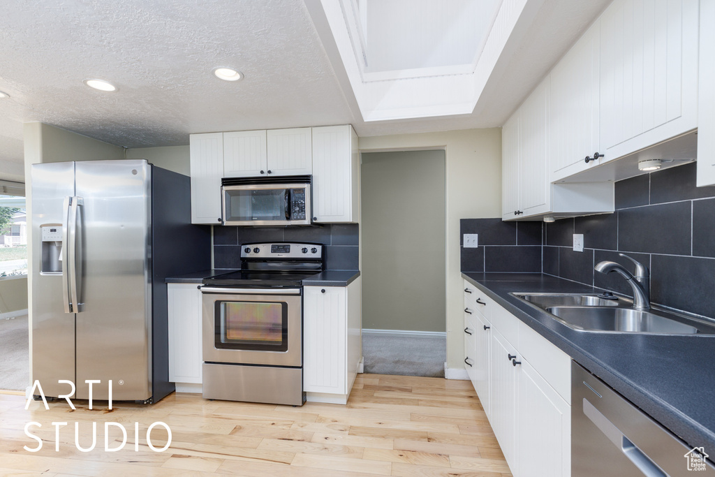 Kitchen featuring stainless steel appliances, a sink, dark countertops, light wood finished floors, and a textured ceiling